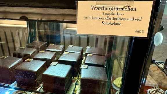 Eine Vitrine mit Kuchen. Auf einem Schild daran steht "Wartburgtürmchen - hausgebacken - mit Himbeer-Butterkrem und viel Schokolade"