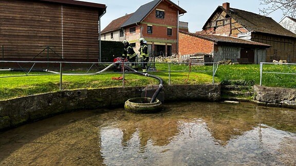 Zwei Feuerwehrleute pumpen Wasser aus einem Teich.