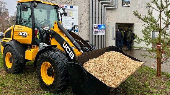 Ein Radlader, dessen Schaufel mit Hackschnitzeln aus Holz gefüllt ist.