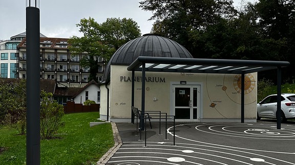 Planetarium Bad Salzungen von außen: hellgelbe Wand, Parkplatz mit Umlaufbahnen bemalt