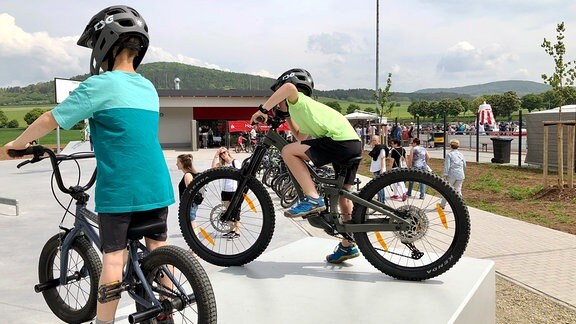 Zwei Kinder mit Mountainbikes auf Skater-Anlage 