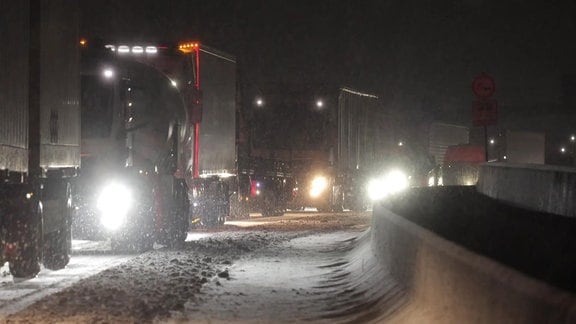 Lkw stehen nachts bei Schneefall im Stau auf der Autobahn