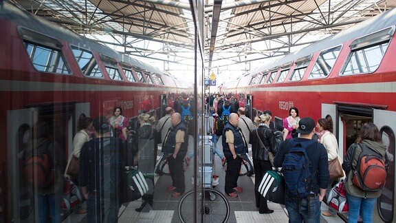 Reisende stehen am 21.05.2015 am Hauptbahnhof in Erfurt (Thüringen) auf einem Bahnsteig vor einem Zug der Deutschen Bahn und spiegeln sich in einer Scheibe.