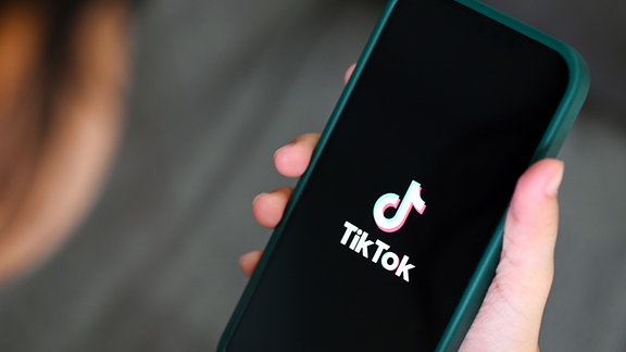 Ein Kind hält ein Smartphone auf dem dal Logo von TikTok zu sehen ist.