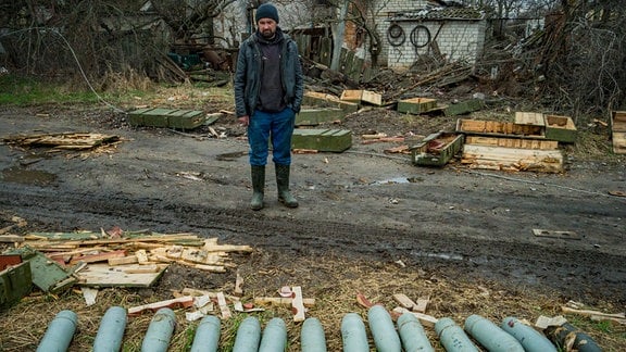 Ein Mann steht hinter aufgereihten Panzergranaten, die die russische Armee bei ihrem Rückzug aus dem Dorf Andrijiwka in der Nähe von Kiew zurückgelassen hat.