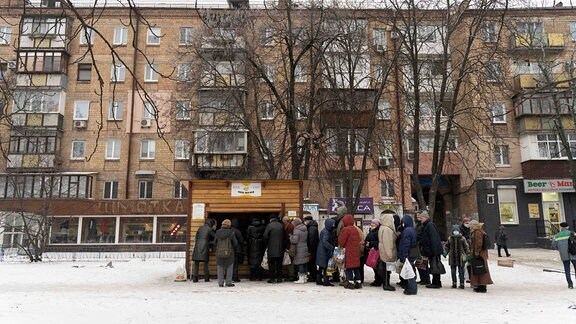 Menschen stehen in Kiew an einer Essensausgabe in einer hölzernen Hütte an.