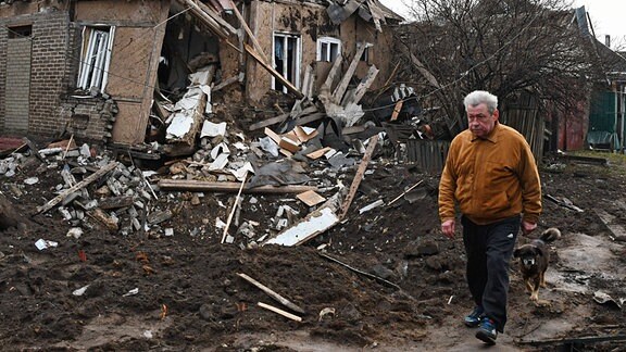 Ein Mann geht spazieren vor einem zerstörten Wohnhaus