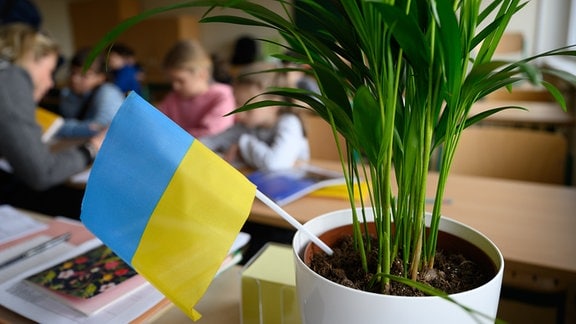 Schüler in einem Klassenzimmer, im Vordergrund eine ukrainische Flagge.