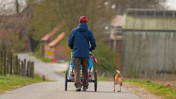 Ein Mann geht mit einem Kinderwagen und einem Hund an der Leine spazieren
