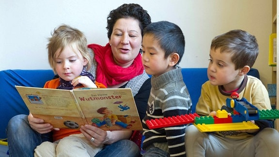 Eine Kindergärtnerin liest den Kinder ein Buch vor.