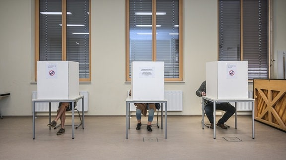 Wähler sitzen im Wahllokal im Gymnasium Rutheneum hinter Wahlkabinen.