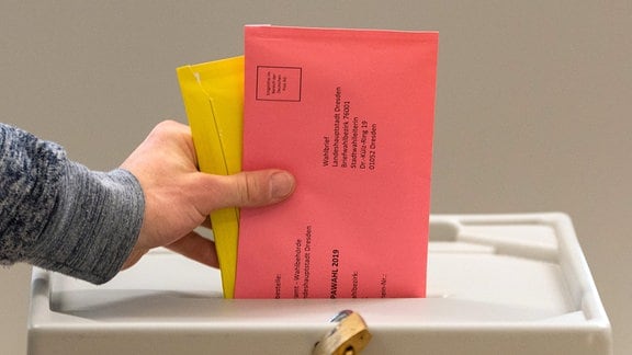 Ein Mann wirft in einem Wahllokal für die Briefwahl zwei Briefumschläge mit den Stimmzetteln in eine Wahlurne