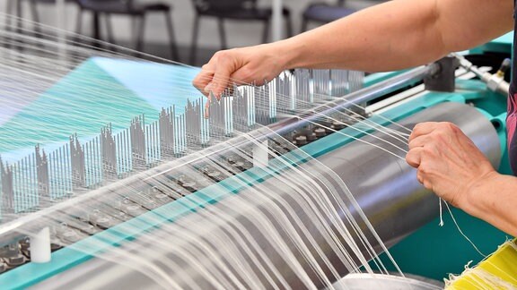 Eine Mitarbeiterin bestückt in einer Textilweberei die sogenannte «Zettelmaschine» mit Garn. 