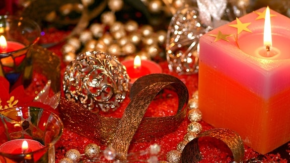 Festliche Weihnachtsdekoration mit Kerze, Teelichten, Kugeln und goldenem Band.