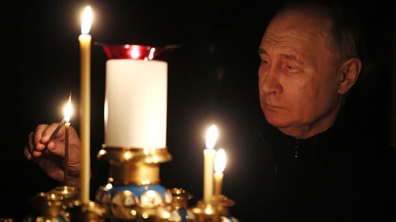 Der russische Präsident Putin entzündet eine Kerze.