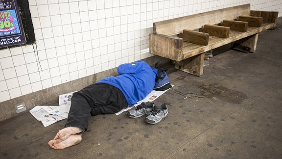 Obdachlose Person schläft in einem U-Bahnhof auf dem Boden.