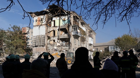 Rettungskräfte und Anwohner stehen vor einem Wohnhaus, das durch einen russischen Luftangriff schwer beschädigt wurde.