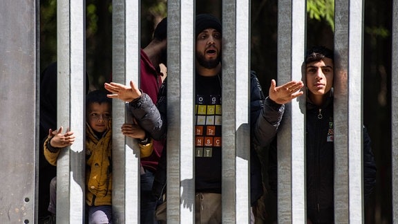 Migranten stehen an einem Eisenzaun
