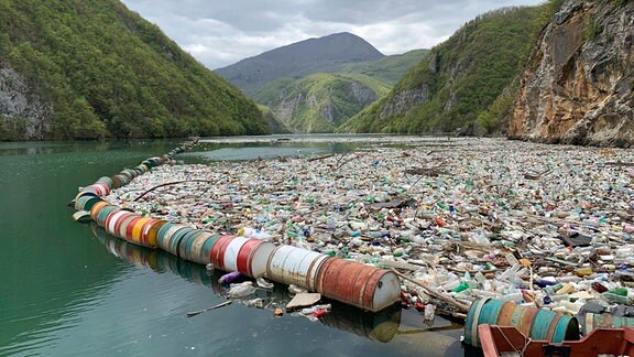 Müll treibt in einem Fluss vor Bergpanorama.