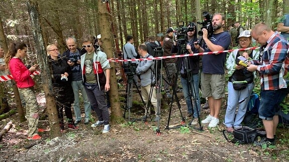 Kamerateams stehen im Wald hinter einer Absperrung