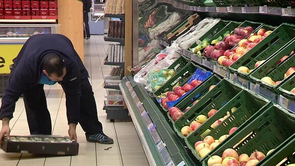 Ein Supermarktangestellter stellt eine Kiste mit Gemüse in ein Regal.
