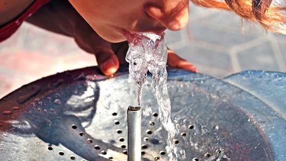 Eine junge Frau trinkt aus einem Brunnen