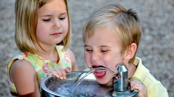 Ein Junge und ein Mädchen trinken aus einem Brunnen
