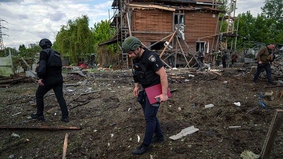 Ukrainische Polizisten suchen nach Fragmenten einer Gleitbombe vor einem beschädigten Haus nach einem russischen Luftangriff auf ein Wohnviertel.