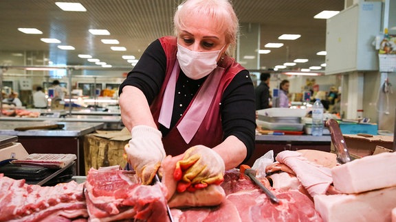 Ein Verkäufer mit Gesichtsmaske und Handschuhen verkauft Fleisch auf einem Lebensmittelmarkt im Schwarzmeerort Sotschi