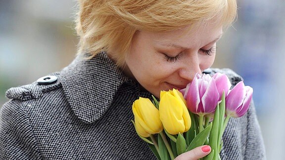 Frau riecht an Blumen.