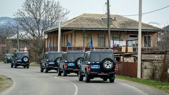 Schwarze Jeeps vor einem Haus, im Hintergrund Berge