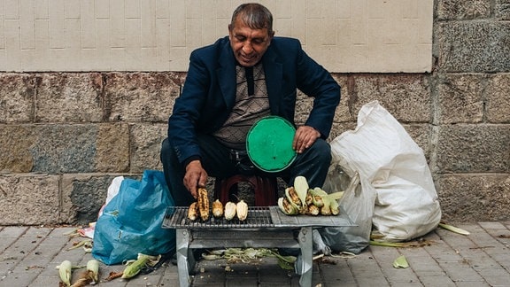 Straßenverkäufer mit gegrillten Maiskolben am Rande des traditionellen Xhiro (Flanieren und Treffen mit Bekannten) in der albanischen Stadt Korça