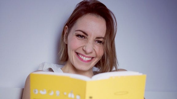 Eine junge Frau sitzt im Bett und liest in einem Buch