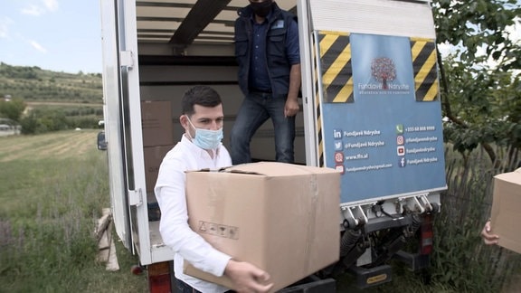 Junger Mann mit Mundschutz entlädt Kisten von einem LKW.