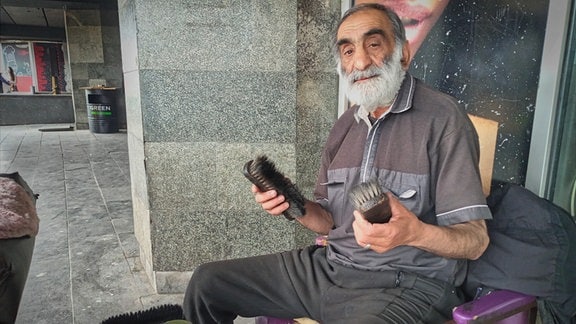 Mischa, ein Schuhputzer aus Tbilissi sitzt vor dem Bahnhof mit zwei Bürsten in der Hand