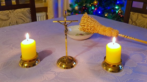 Kruzifix mit zwei Kerzen und einem Weihwasserwedel.