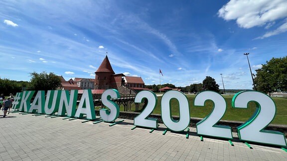 Auf einem asphaltierten Platz stehen bei Tag Leuchtbuchstaben, aus denen die Wort-Folge Kaunas 2022 gebildet wurde.
