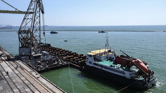 Arbeiter laden in Hafen von Mariupol Bleche auf ein Schiff.