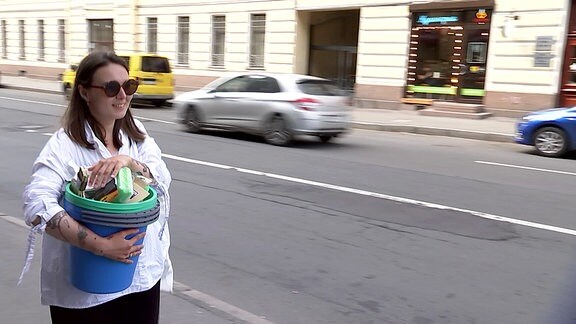 Eine Frau mit Eimer im Arm auf einer Straße.