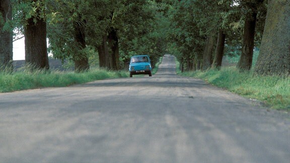 Blaues Auto fährt einsam auf einer Allee in Dubliny, Polen.