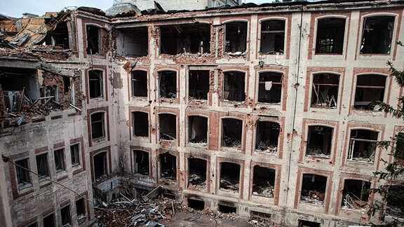 Blick auf ein zerstörtes Auzto und die komplatt entglaste Hausfront im Hinterhof der Universität Charkiw.