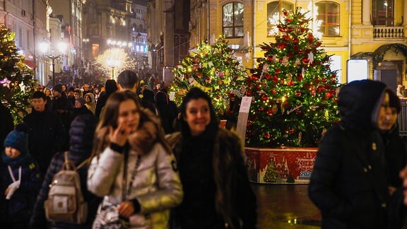 Menschen gehen an geschmückten Weihnachtsbäumen vorbei