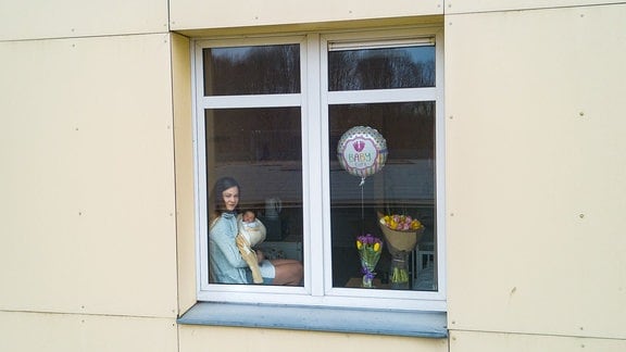 Eine Frau mit Baby im Arm sitzt am Fenster