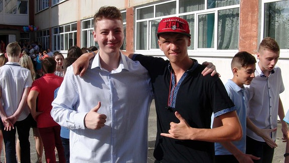 Zwei Jugendliche posieren mit Handzeichen für Kamera. 