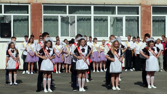 Mädchen in festlicher Kleidung tanzen synchron auf einem Schulhof. 
