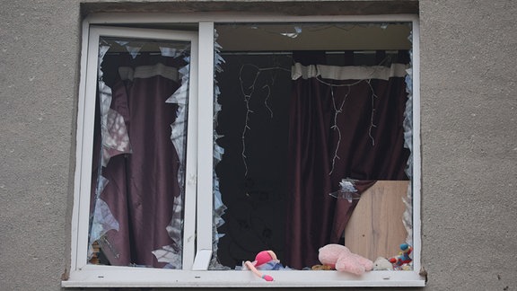 Kuscheltiere und Spielzeug sind an einem zerborstenem Fenster zu sehen.