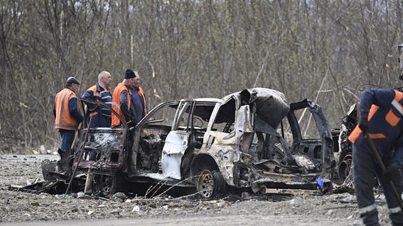 Hilfskräfte untersuchen ein ausgebranntes Autowrack nach einem russischen Angriff. 