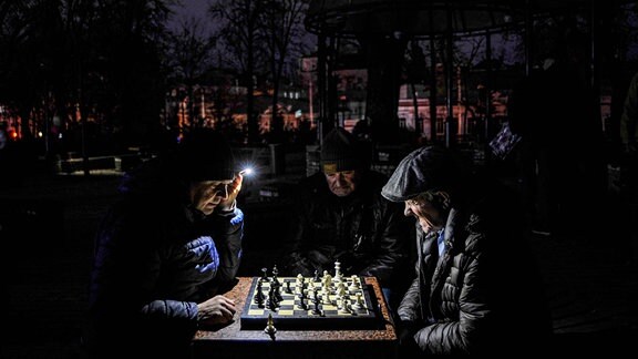 Männer spielen in einem Park in Kiew bei Taschenlampenlicht Schach