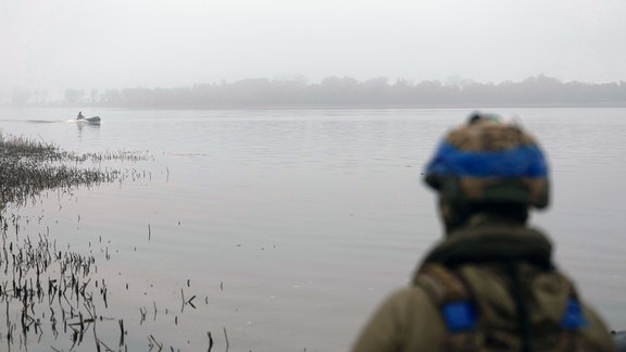 Ein ukrainischer Soldat beobachtet seinen Kameraden, wie er am Samstag, 14. Oktober 2023, auf dem Boot an der Frontlinie in der Nähe von Cherson, Ukraine, durch den Fluss Dnipro segelt.
