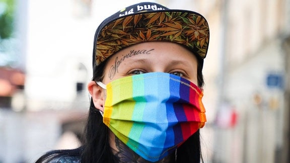 Junge Frau mit Tattoos und Regenbogen-Mundschutz
